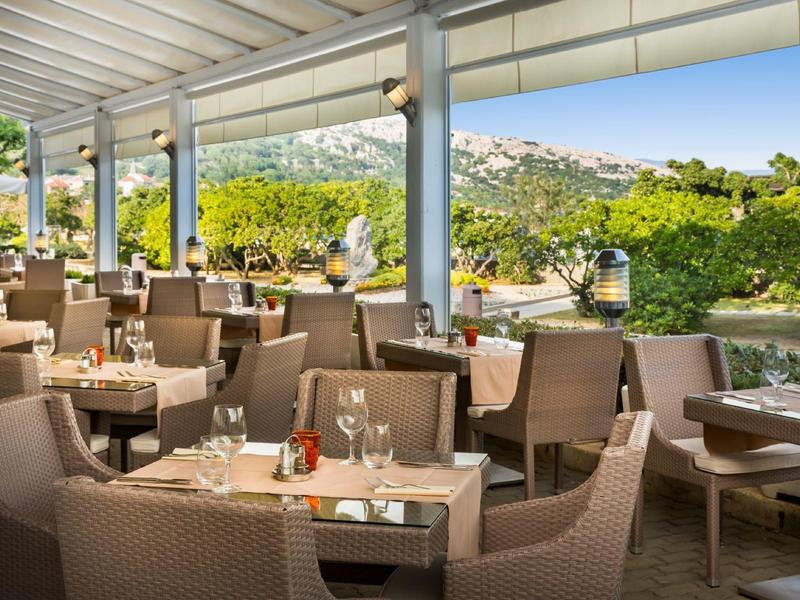 Terrasse extérieure couverte d'un restaurant avec mobilier en rotin et vue sur un paysage vallonné.
