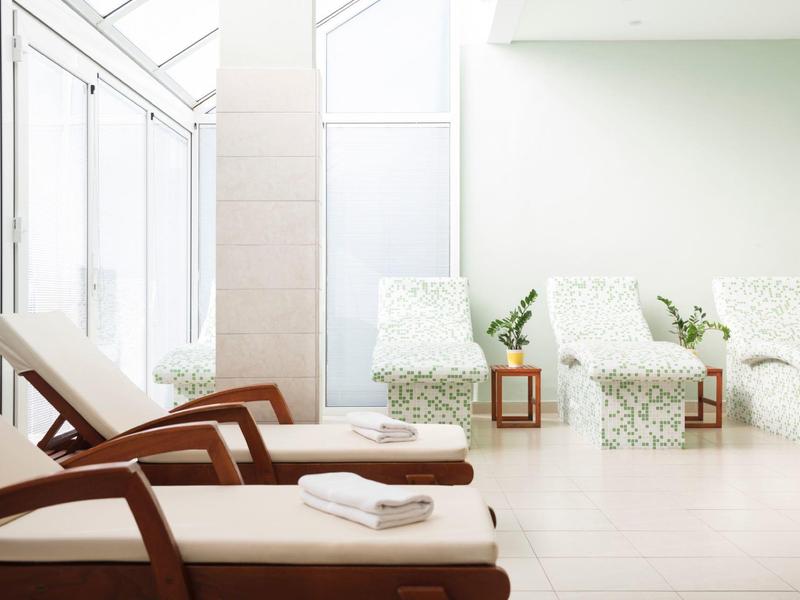 Espace de détente lumineux et minimaliste avec des chaises longues et des fauteuils rembourrés près de grandes fenêtres.