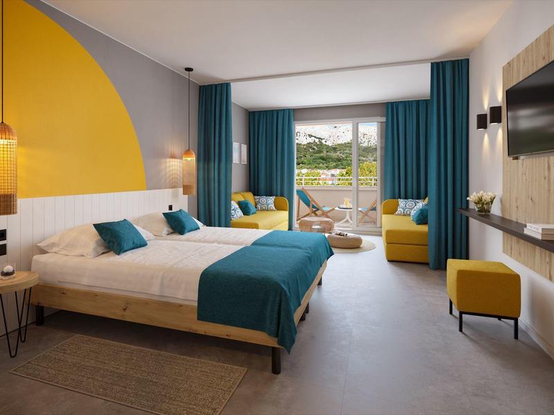 Chambre d'hôtel moderne avec lit double, rideaux turquoise et coin salon confortable.