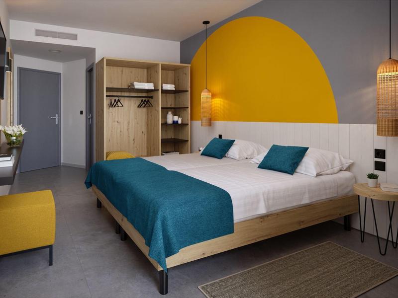 Chambre d'hôtel moderne avec grand lit, couvre-lit bleu et mur d'accent jaune.