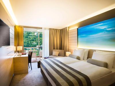 Modernes Hotelzimmer mit zwei Einzelbetten, großem Fenster und ruhiger Atmosphäre.