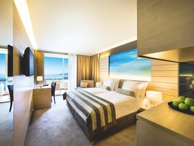 Chambre d'hôtel moderne avec grand lit, bureau, télévision et vue panoramique sur la mer.