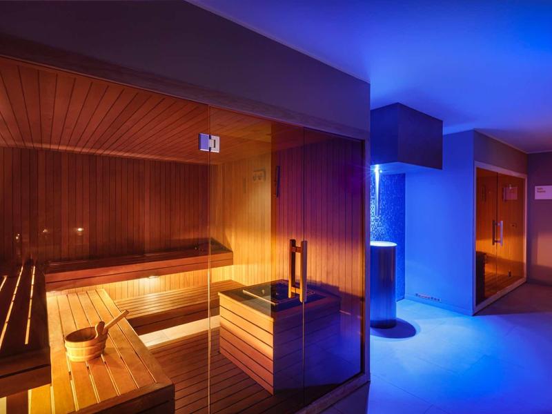 Modern sauna area with wooden benches and atmospheric blue lighting.