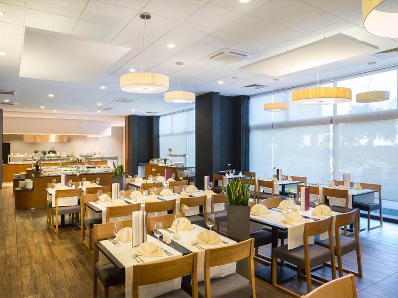 Modern restaurant with wooden furniture, large windows, and warm lighting.