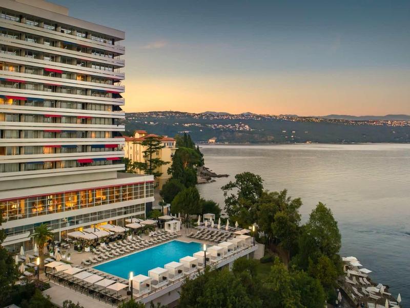 Hotel with large pool and terrace by the water at sunset.
