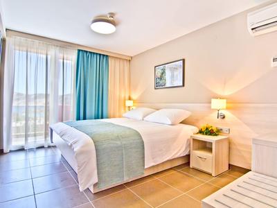 Licht hotelkamer met groot bed, nachtlampjes en balkon met gordijnen.