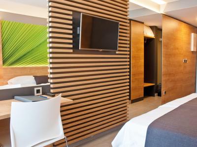 Modernes Hotelzimmer mit Holzwand, TV, weißem Stuhl, Bett und stilvoller Beleuchtung.