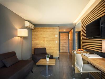 Modern eingerichtetes Hotelzimmer mit Holzwänden, braunen Sofas und großem Fernseher an der Wand.