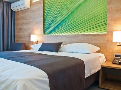 Modernes Schlafzimmer mit großem Bett, weißen Bettwäsche, brauner Decke und grün-blauem Wandbild.