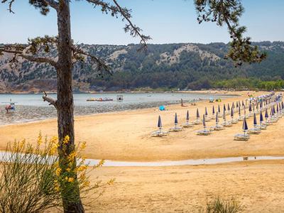 Breed zandstrand met gesloten parasols en kalm water voor beboste heuvels.