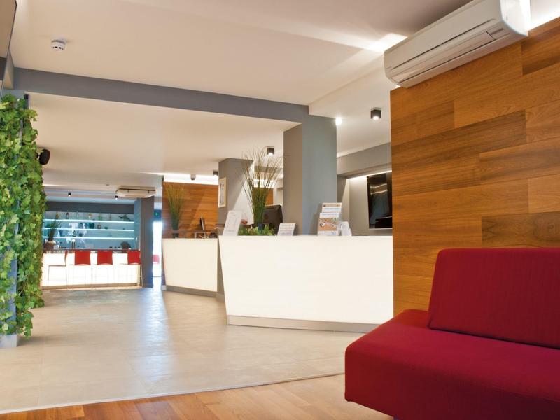 Moderne Empfangshalle mit rotem Sofa, weißen Tresen, Holzverkleidung und grünem Pflanzenvorhang.