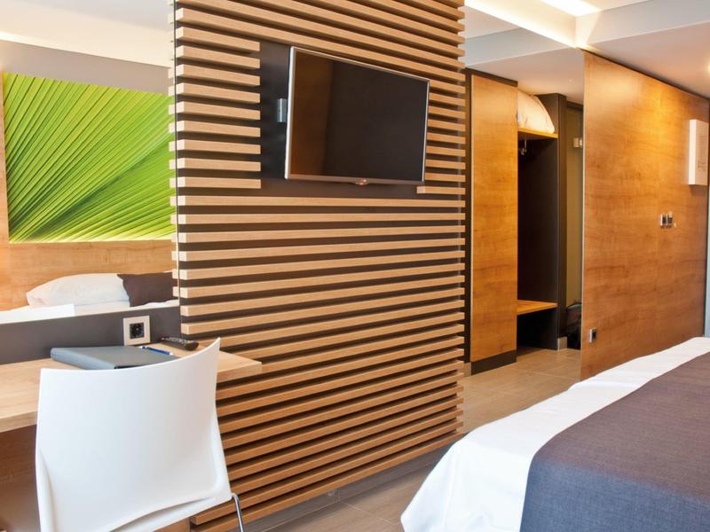 Modernes Hotelzimmer mit Holzwand, TV, weißem Stuhl, Bett und stilvoller Beleuchtung.