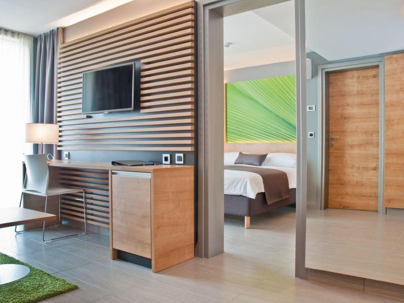 Moderner Hotelraum mit Holzvertäfelung, Bett, großem Spiegel und Fernseher an der Wand.