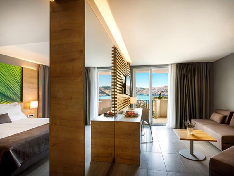 Modern eingerichtetes Hotelzimmer mit Bett, Sofa, Holzmöbeln und großem Fenster mit Ausblick.