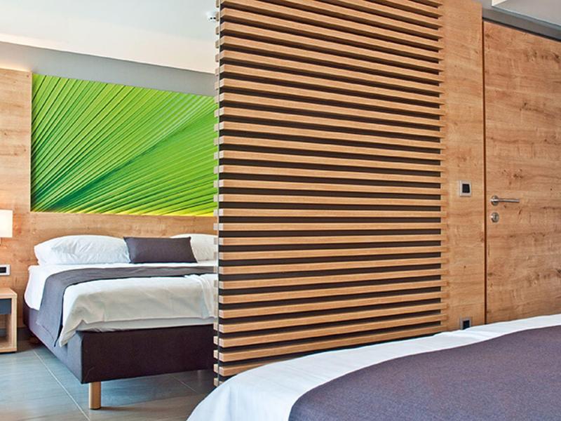 Moderner Schlafraum mit Holzlammellenwand, Doppelbett, grünem Wandbild und schlichter Lampe.