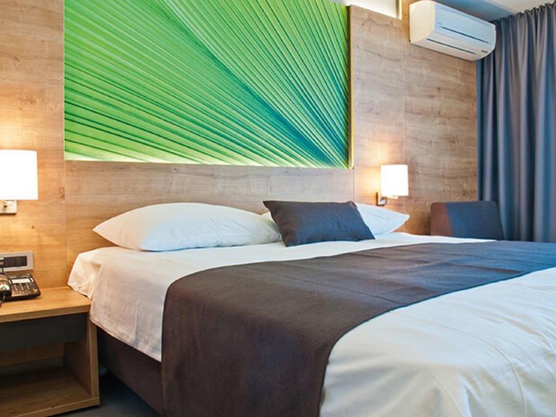 Modernes Schlafzimmer mit Holzwand, großem Bett, weißer Bettwäsche und grünem Wandbild.