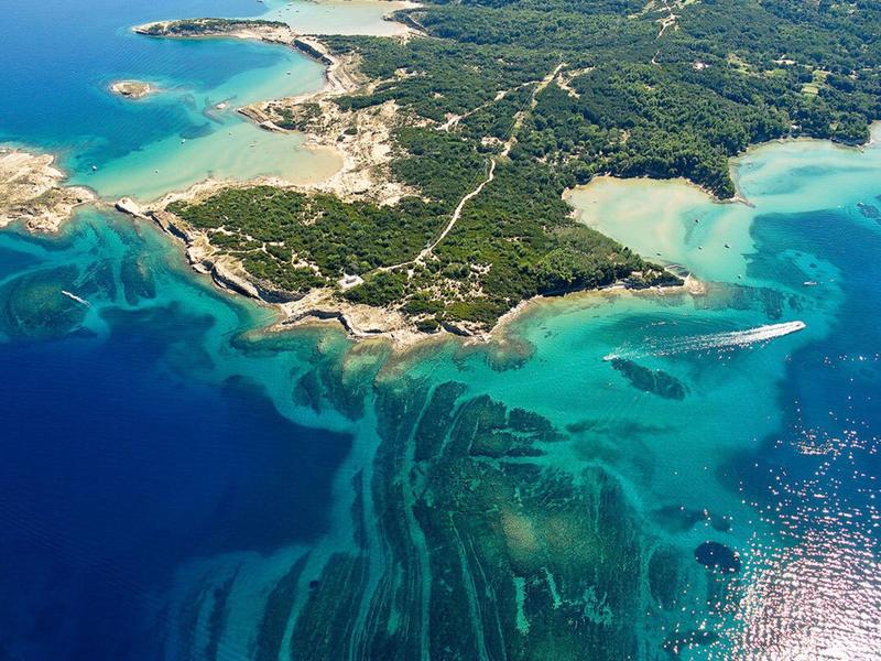 Luftaufnahme einer bewaldeten Halbinsel mit klarem blauem Wasser und verschiedenen Tiefenstufen.