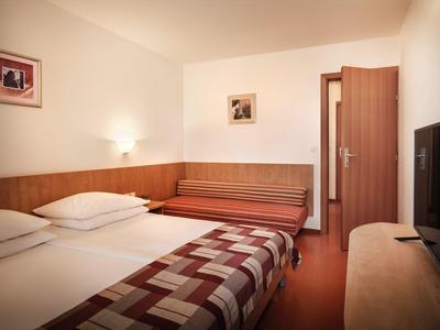 Ein einfaches Hotelzimmer mit Doppelbett, Fernseher und einer offenen Tür.