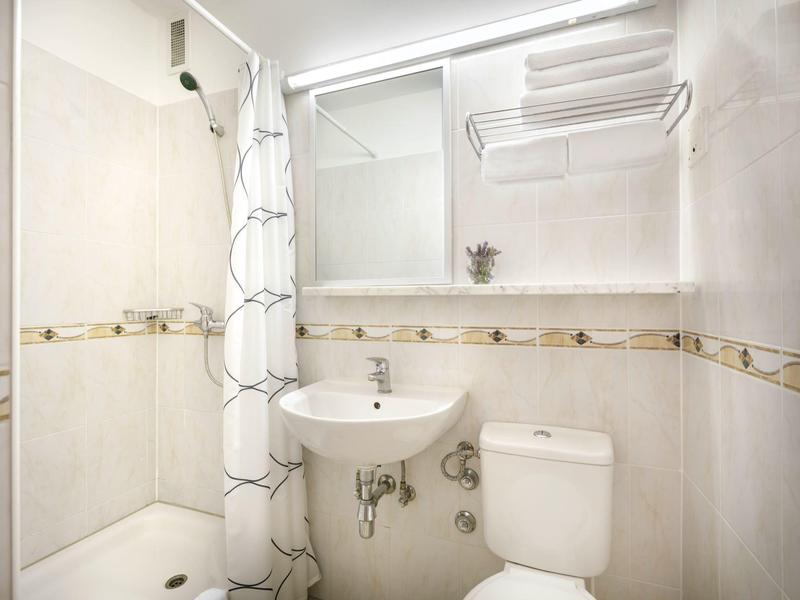 Kleines weiß gefliestes Badezimmer mit Dusche, Waschbecken, Toilette und Handtuchhalter.