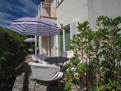 Terrasse mit Tisch, Stühlen und gestreiftem Sonnenschirm neben einem weißen Gebäude.