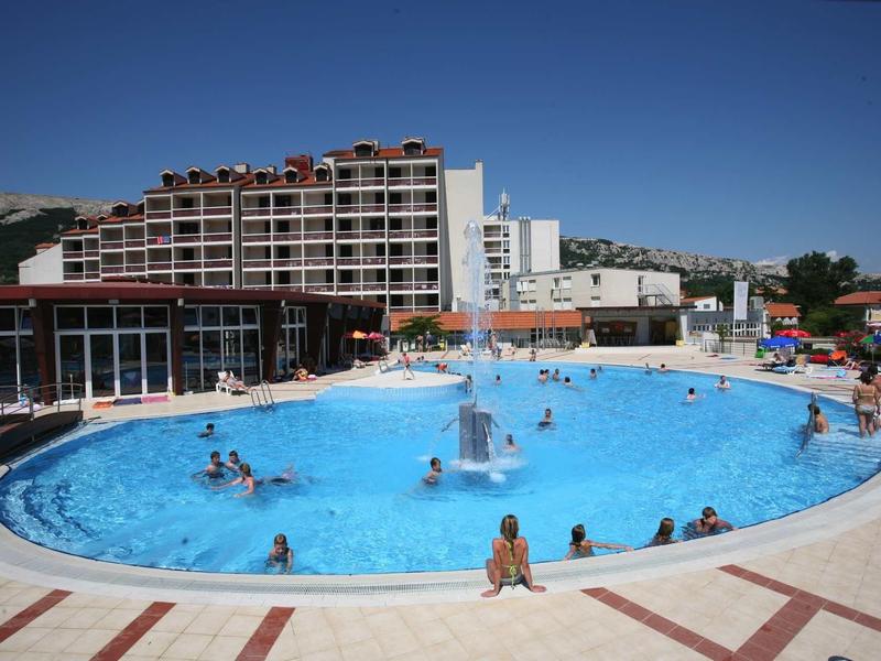 Grande piscina all'aperto con persone e un edificio dell'hotel sullo sfondo sotto un cielo blu.