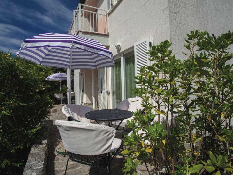 Terrazza con sedie, tavolo e ombrellone accanto a un edificio dell'hotel sotto un cielo azzurro.