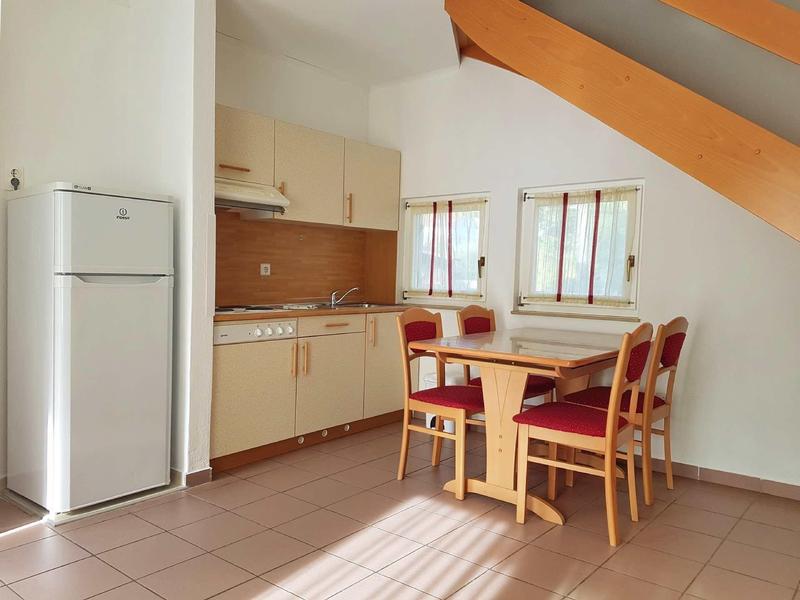 Piccola cucina con tavolo da pranzo e quattro sedie in una stanza luminosa con soffitto inclinato.