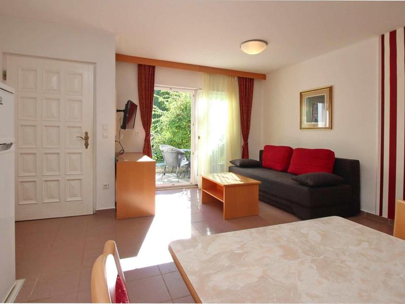 Camera d'albergo luminosa con divano, tavolo, sedie e accesso a terrazza con vista giardino.