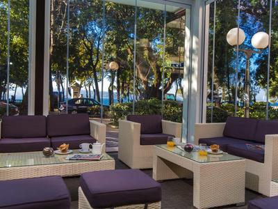 Moderne Lounge mit lila Polstermöbeln, weißen Tischen und großen Fenstern zu Bäumen draußen.