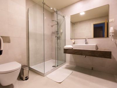 Salle de bains d'hôtel moderne avec douche à l'italienne, toilettes et lavabo avec grand miroir.