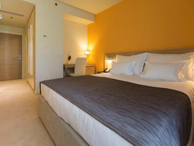 Chambre d'hôtel moderne avec grand lit, bureau et mur jaune en arrière-plan.