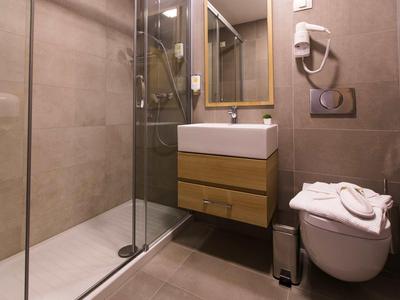 Salle de bain moderne avec douche en verre, lavabo mural et toilettes suspendues.