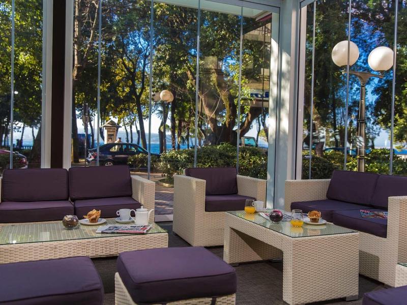 Modern lounge area with sofas and glass walls, surrounded by trees and lanterns.