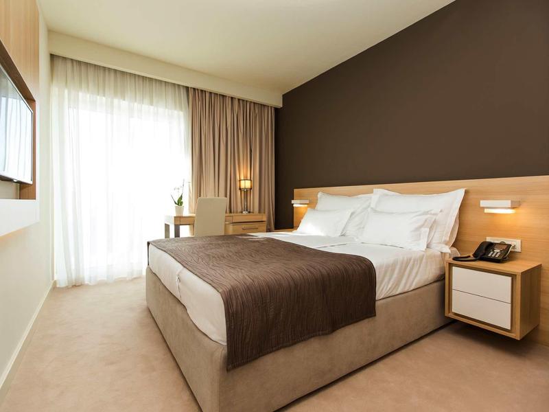 Modern hotel room with double bed, brown accents, and large window with curtains.