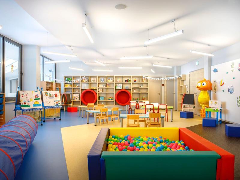 Bright kids' playroom with colorful ball pit, chairs, and toy shelves in a hotel or daycare setting.