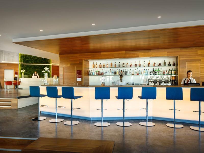 Modern hotel bar with white counter, blue bar stools, and a bartender preparing drinks.