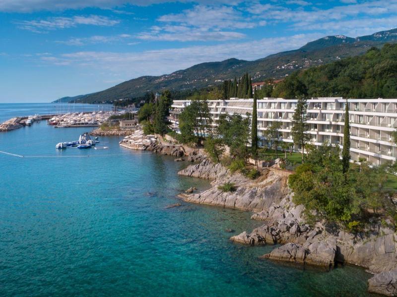 Coastal hotel nestled by rocky shoreline with lush greenery and calm blue sea.