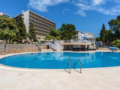 Runder Hotelpool mit blauer Wasserfläche und umliegenden Bäumen und Gebäuden bei klarem Himmel.