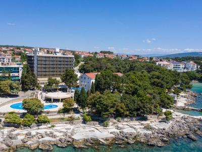 Hotelanlage am felsigen Küstenabschnitt mit Pool und grünen Bäumen neben dem Meer.