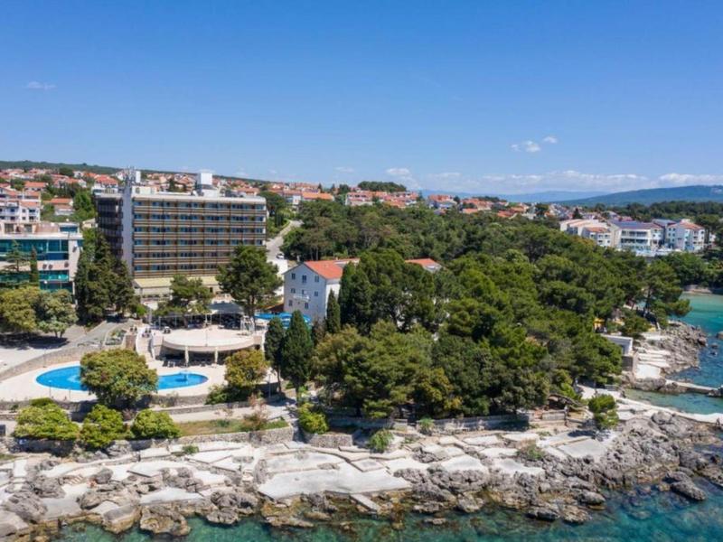 Hotelanlage am felsigen Küstenabschnitt mit Pool und grünen Bäumen neben dem Meer.