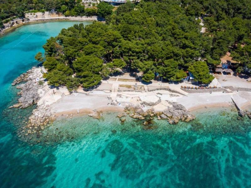 Luftaufnahme einer bewaldeten Küste mit klarem türkisfarbenem Wasser und Sandstrand.