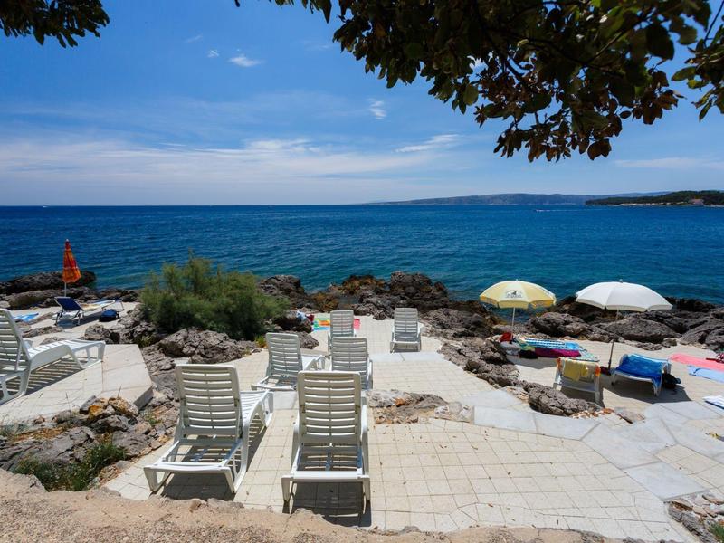 Sonnenliegen und Sonnenschirme an der felsigen Küste mit Blick auf das Meer unter blauem Himmel.