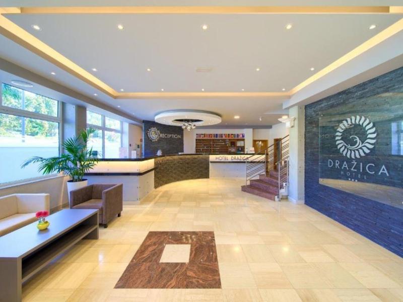 Helle Hotellobby mit Sitzbereich, Rezeption und großen Fenstern mit Blick nach draußen.