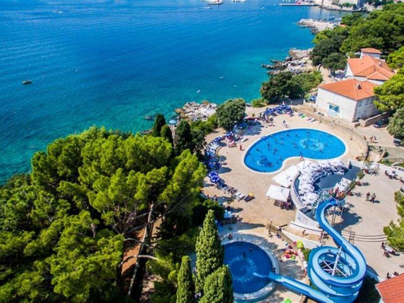 Blick auf Hotelpool mit Wasserrutsche, umgeben von Bäumen und am Meer gelegen.