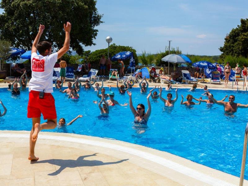 Person animiert eine Gruppe von Menschen im Pool zu bewegen, umgeben von Sonnenschirmen und Bäumen.