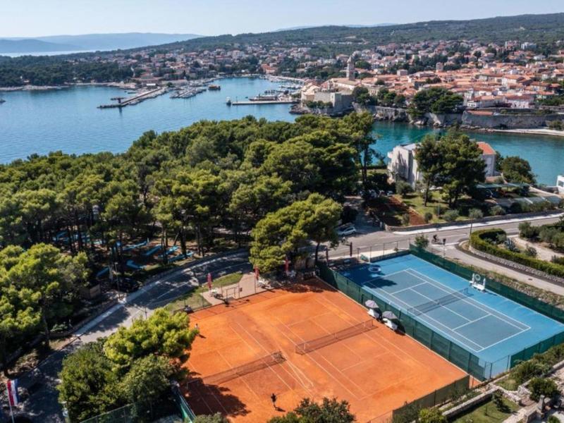 Blick auf Tennisplätze am Meer mit Stadt und Hügeln im Hintergrund