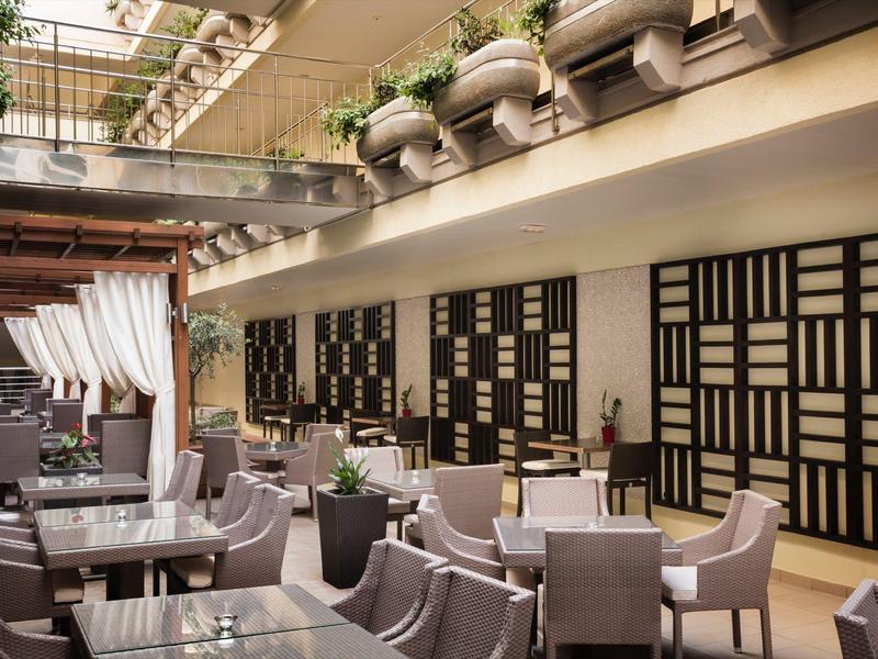 Restaurant moderne et élégant avec tons gris, accents en bois et plantes dans une cour cosy.