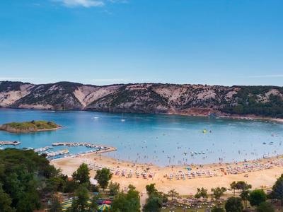 Beach with golden sand and clear blue water in front of rocky hills and a blue sky.