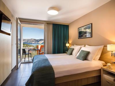 Habitación de hotel acogedora con cama doble, balcón y vista al paisaje en luz diurna.