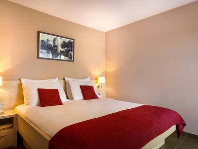 Habitación de hotel acogedora con cama doble, ropa blanca, acentos rojos y dos lámparas de noche.